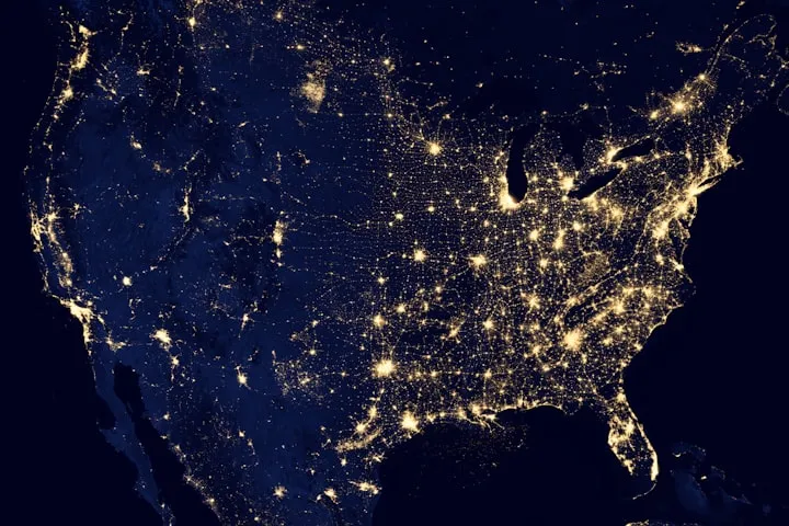 Satellite view of the contiguous United States at night, showing glowing city lights against a dark Earth
