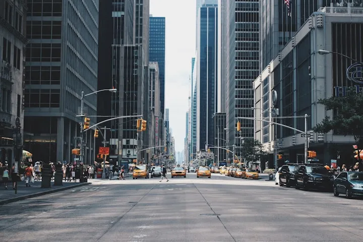 Wide one-point perspective down a Manhattan avenue lined with skyscrapers and yellow taxis