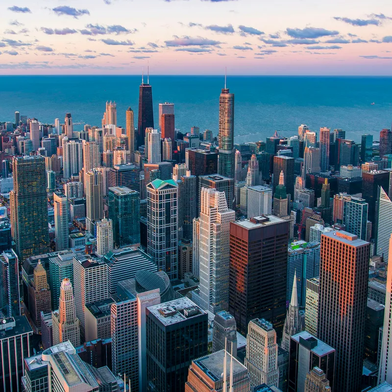Aerial view of the Chicago skyline beside Lake Michigan under a pink and purple sunset sky
