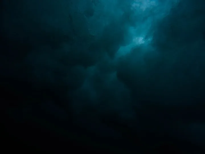 Underwater view looking up at churning white bubbles and dark teal water beneath a crashing wave