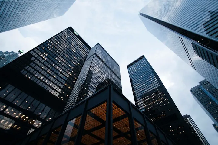 Low-angle view looking straight up at dark glass skyscrapers against a pale overcast sky