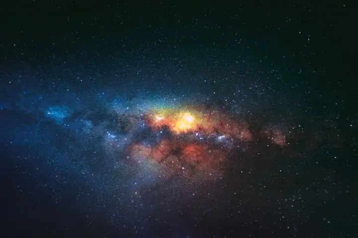 Long-exposure photograph of the Milky Way galactic core with yellow, orange, and blue star clouds