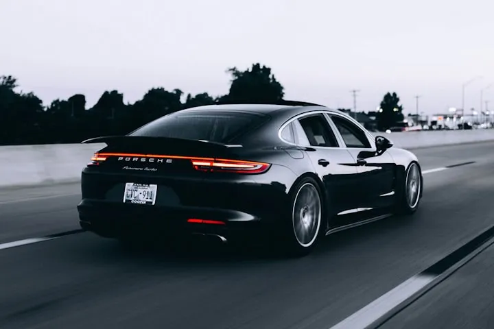 Dark Porsche Panamera Turbo driving on a highway at twilight, rear three-quarter view with motion blur