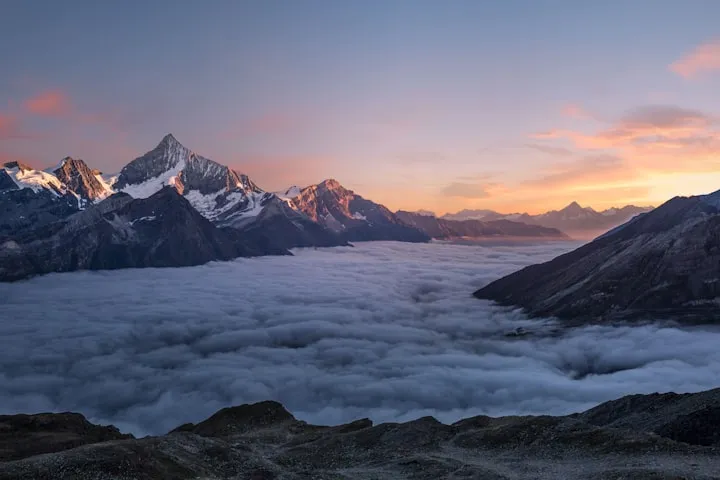 Snow-dusted mountain peaks rising above a thick sea of clouds at sunrise