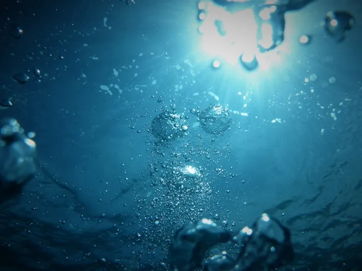 Underwater view looking up at the sun with air bubbles rising through deep blue water