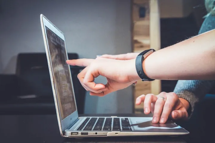 Two people collaborating at a silver laptop, one pointing at the screen and the other near the trackpad