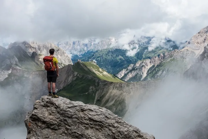 Hiker with a red backpack standing on a rocky ledge overlooking misty mountain peaks