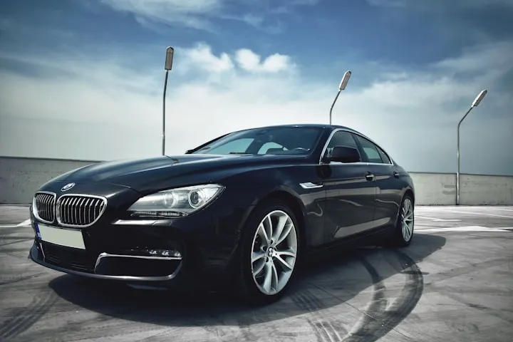 Front three-quarter view of a black BMW sedan on a concrete rooftop with circular tire skid marks and a blue sky