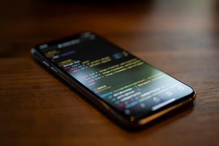 Smartphone on a wooden table displaying syntax-highlighted code in a dark editor theme