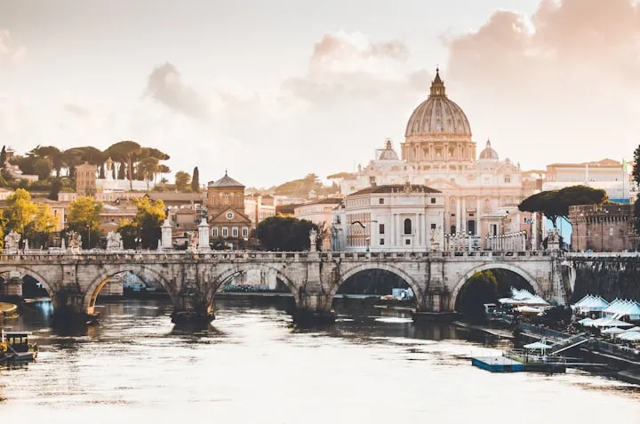 Tiber River in Rome with Ponte Sant'Angelo and the dome of St. Peter's Basilica under a warm sunset sky