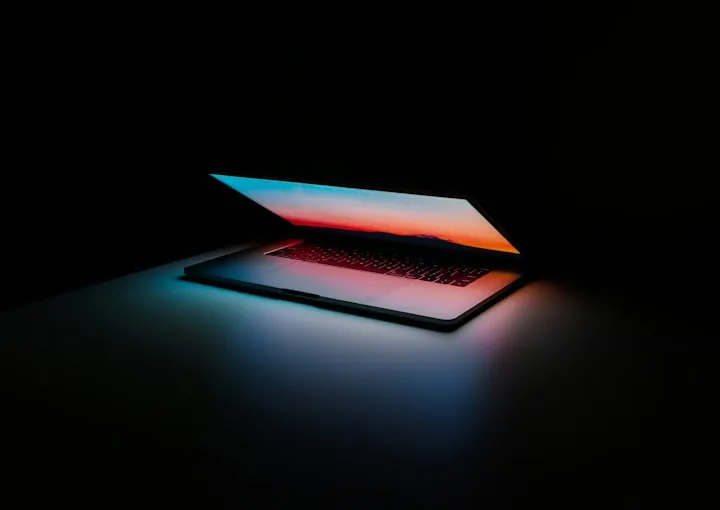 Partially open laptop in a dark room, its screen showing a sunset that lights the keyboard