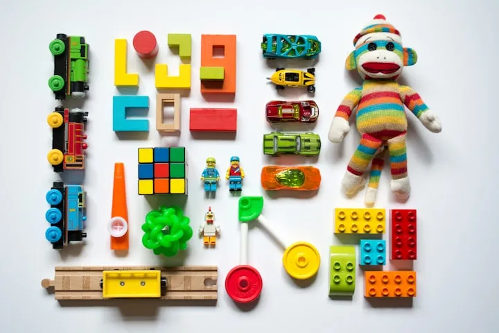 Overhead flat-lay of colorful children's toys including trains, cars, blocks, a Rubik's cube, and a sock monkey