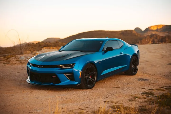 Bright blue Chevrolet Camaro SS with a black hood parked on a desert dirt road at sunset