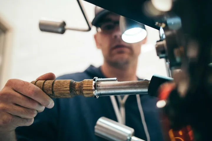 Close-up of a hand pulling a coffee-bean trier from a professional roasting machine