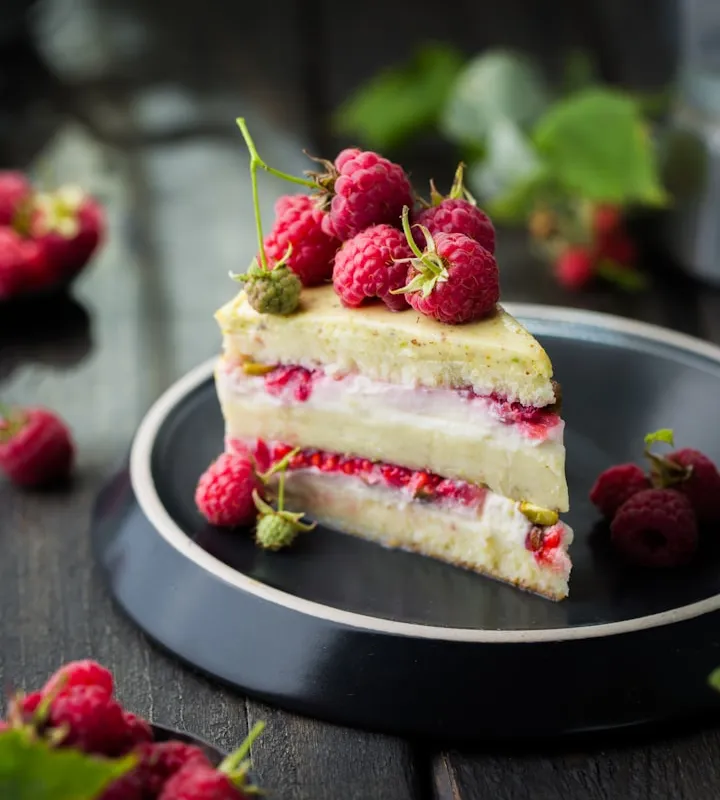 Slice of layered sponge cake topped with fresh raspberries on a dark plate