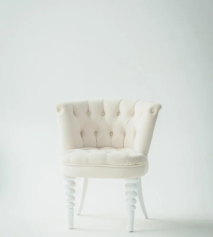 Cream button-tufted armchair with decorative white turned legs against a plain light gray studio background