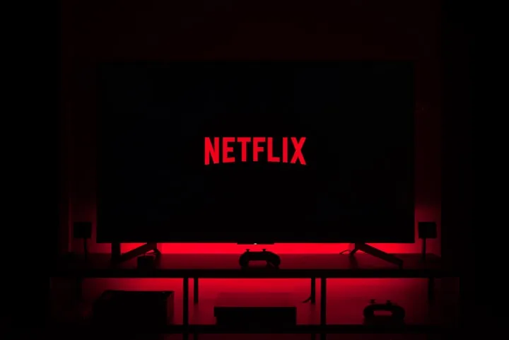 Television in a dark room displaying the red Netflix logo with red ambient backlighting