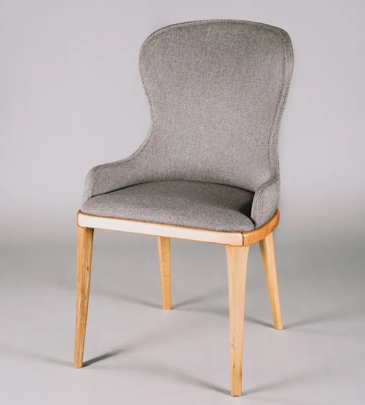 Studio photo of a modern grey upholstered chair with a high back and light wooden tapered legs