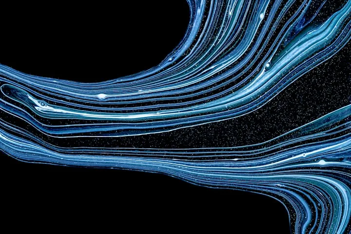 Abstract macro of swirling light blue and white liquid paint lines against a black background